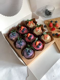 a box filled with cupcakes covered in frosting and topped with fresh fruit