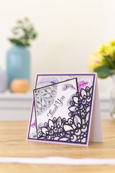 a close up of a greeting card on a table with flowers in the back ground