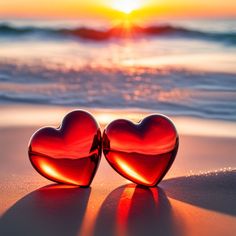 two red heart shaped glasses sitting on top of a sandy beach next to the ocean