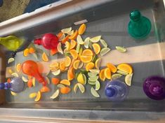 several different colored cups and spoons on a metal tray with orange peels, lemons, and limes