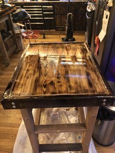 a wooden table sitting on top of a hard wood floor next to a metal trash can