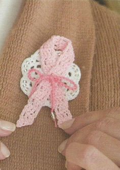 someone is holding a pink crochet bow on their sweaters and it looks like they are knitting