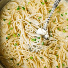 a silver bowl filled with pasta and topped with parmesan cheese, scallions and chives