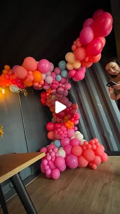 a woman standing next to a table holding a cell phone in front of a bunch of balloons