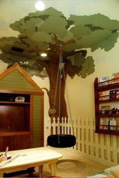 a room with a tree painted on the wall and a swing set in front of it