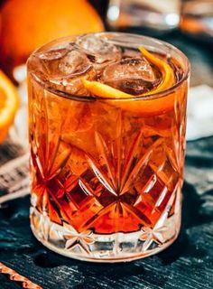 a close up of a drink in a glass on a table with oranges behind it