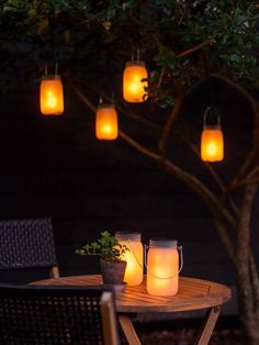 mason jar lights hanging from a tree over a table with chairs and potted plant