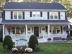 a white house with black shutters and flowers in the front yard on a sunny day