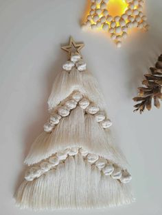 a white christmas tree made out of yarn and pine cones next to a wall light