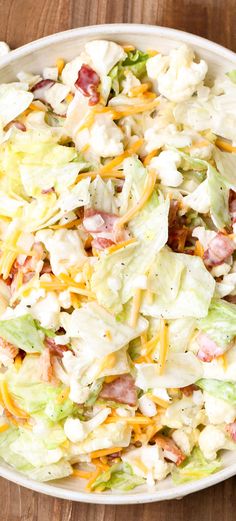 a salad with lettuce, bacon and cheese in a white bowl on a wooden table