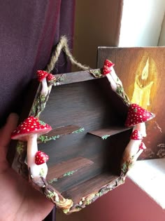 a person holding up a birdhouse made out of wood and red mushrooms on it