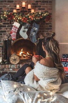 a woman sitting on a bed in front of a fire place with stockings hanging over it