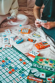 two people sitting on a bed playing games with their hands and holding game pieces in front of them