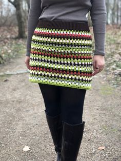 a woman in black boots is standing on the ground wearing a green and red crochet skirt