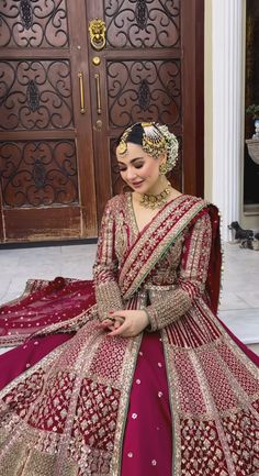 a woman in a red and gold bridal gown sitting on the ground with her hands together