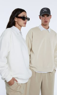 two people standing next to each other in front of a white background wearing sunglasses and sweatshirts