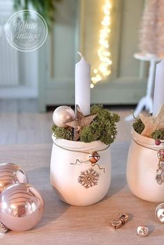 two white vases filled with plants and candles on top of a table next to other decorations