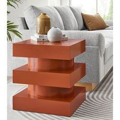 a living room with a couch and a table in front of the couch is an orange three tiered end table