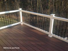 a deck with white railings and wood flooring in front of some trees on the other side