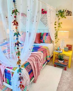 a bed with white drapes and pink bedspread on top of it next to a yellow table