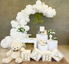 a teddy bear sitting on the floor in front of balloons and letters that spell out baby