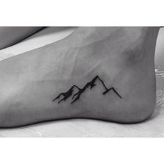 a black and white photo of a foot with a mountain tattoo design on it's side