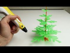 a hand holding a pen writing on a piece of paper next to a miniature christmas tree