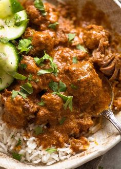 a white plate topped with rice and meat next to cucumbers