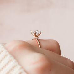 a woman's hand holding a ring with a heart shaped diamond on it, in front of a pink background