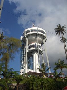 a tall white tower sitting on the side of a lush green hillside next to palm trees