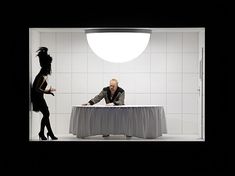 a man and woman sitting at a table in front of a white wall with black tiles