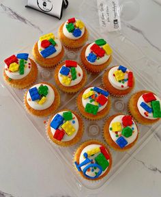 cupcakes decorated with lego pieces on a clear plastic tray next to a camera