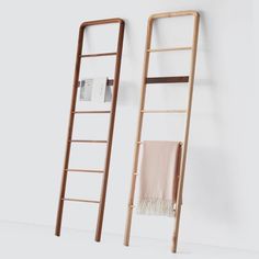 two wooden ladders next to each other against a white wall with a towel hanging on it