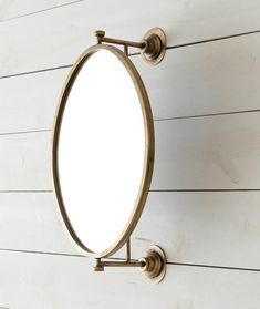 an oval mirror mounted to the side of a white wall with wood planks behind it