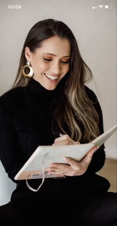 a woman sitting on a chair and smiling while holding an open book in her hands