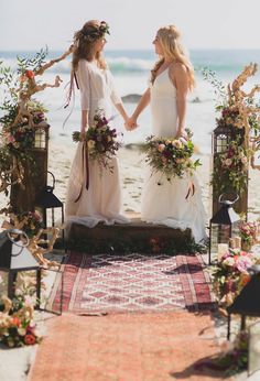 two women standing next to each other holding hands on top of a rug near the ocean