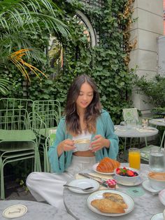 a woman sitting at an outdoor table with food and drinks in front of her,