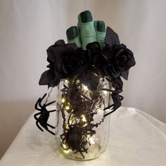 a vase filled with black flowers and lights on top of a white cloth covered table