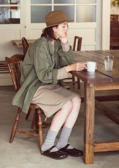 a woman sitting at a table with a coffee cup in her hand and wearing a hat