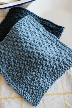 two crocheted pieces of cloth sitting on top of a table next to a bowl