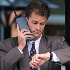 a man in a suit and tie is talking on a cell phone while looking at his watch