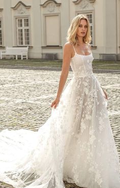 a woman in a white wedding dress standing on a cobblestone road with a building in the background