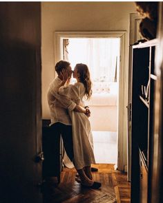 a man and woman embracing each other in front of an open door at the end of a hallway