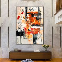 an abstract painting hangs on the wall above a wooden table with flowers in vases