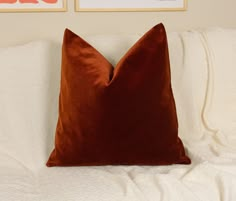 a brown pillow sitting on top of a white bed next to two framed pictures above it