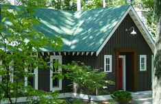 a small house with a green roof and white trim on the front door is surrounded by trees