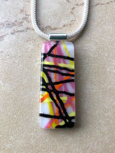 This is a fun fused glass pendant necklace, with opalescent in pink, white, black, yellow and orange. The pendant is approximately .75" x 1.75" and  comes on a 16" mesh choker with lobster clasp. Other pieces available separately.  Caring for fused glass jewelry: To clean, use a soft cloth. Do not use harsh chemicals to clean. Should not be submerged in water, and should be removed when bathing. While fused glass is much stronger, use care when handling as can still break if dropped on hard surface.  Please contact me with any questions, changes or modifications.  Thank you so much for stopping at my shop! Fused Glass Art Jewelry, Fused Glass Pendant Necklace, Fused Glass Necklace, Art Glass Jewelry, Glass Fusion Ideas, Fused Glass Artwork, Glass Craft, Glass Fusion, Fused Glass Pendant