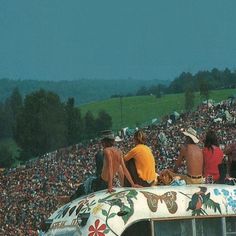 three people sitting on top of an old car in front of a large crowd at a music festival