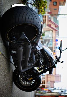 a black motorcycle parked on the side of a building next to a wall with a plant growing out of it