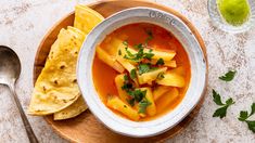 a bowl of soup with tortilla chips next to it on a wooden plate